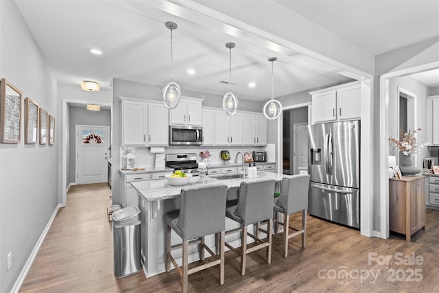 kitchen featuring white cabinetry, stainless steel appliances, hanging light fixtures, and a center island with sink