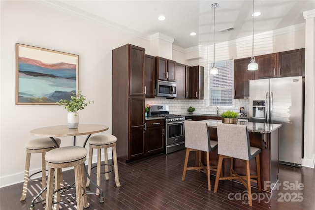 kitchen featuring hanging light fixtures, backsplash, stainless steel appliances, dark hardwood / wood-style floors, and a kitchen breakfast bar