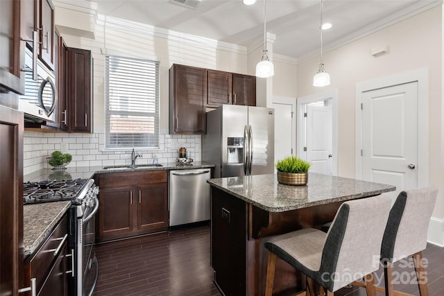 kitchen with sink, a center island, hanging light fixtures, dark stone countertops, and appliances with stainless steel finishes