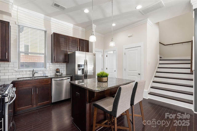 kitchen with appliances with stainless steel finishes, decorative light fixtures, sink, dark stone counters, and a center island