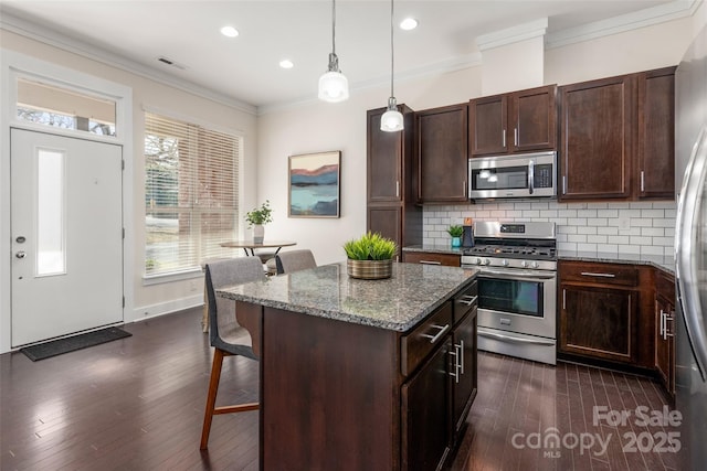 kitchen with a breakfast bar, appliances with stainless steel finishes, dark stone countertops, ornamental molding, and a kitchen island