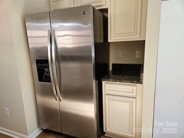 kitchen featuring cream cabinets, stainless steel fridge, baseboards, and dark stone countertops