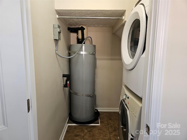 washroom with stacked washer and dryer, laundry area, dark tile patterned floors, and baseboards