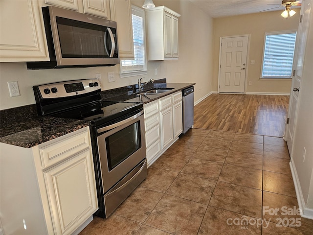 kitchen featuring light tile patterned floors, dark stone counters, ceiling fan, stainless steel appliances, and a sink