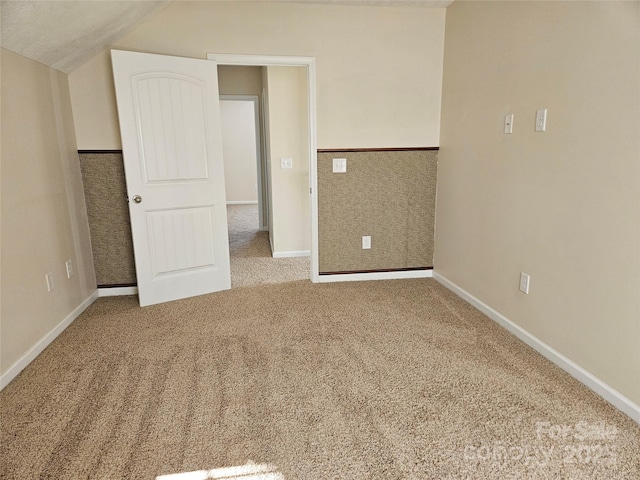 unfurnished bedroom with lofted ceiling, a wainscoted wall, carpet, and baseboards