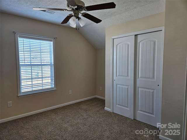 unfurnished bedroom with a textured ceiling, lofted ceiling, baseboards, a closet, and dark colored carpet