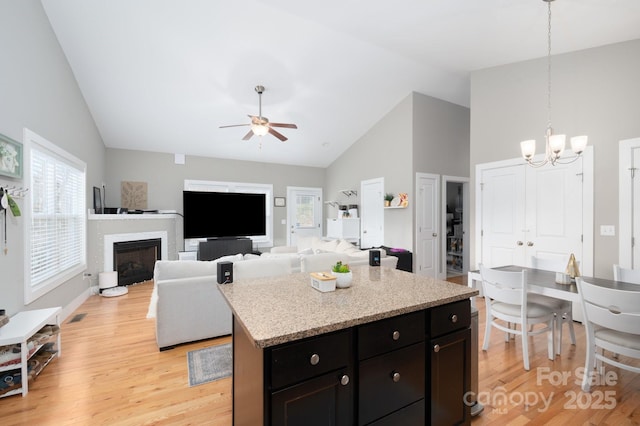 kitchen featuring pendant lighting, high vaulted ceiling, a kitchen island, ceiling fan with notable chandelier, and light wood-type flooring