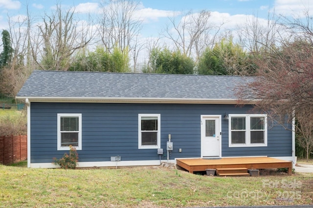 back of house featuring roof with shingles and a lawn