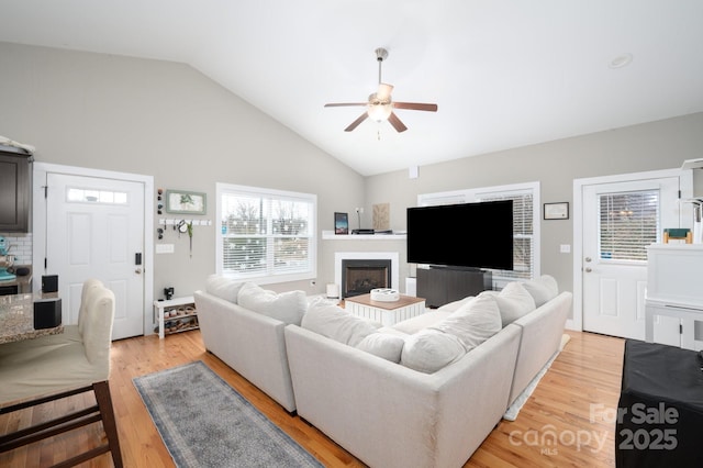 living area featuring light wood-style floors, a fireplace, high vaulted ceiling, and a ceiling fan