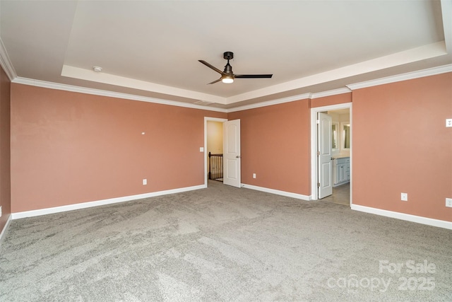 unfurnished bedroom with ceiling fan, ensuite bathroom, a tray ceiling, ornamental molding, and light colored carpet