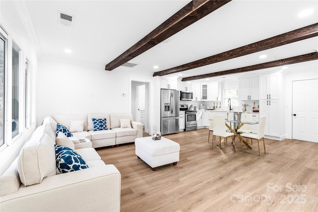 living room with ornamental molding, beam ceiling, sink, and light wood-type flooring