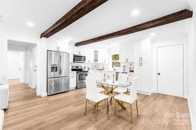 kitchen with beamed ceiling, stainless steel appliances, white cabinets, and light wood-type flooring