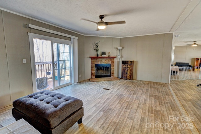 living room with ceiling fan, a fireplace, a textured ceiling, and light wood-type flooring