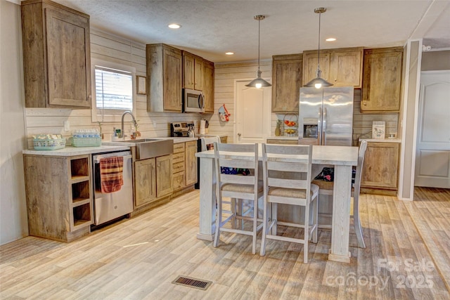 kitchen featuring sink, hanging light fixtures, stainless steel appliances, a center island, and light wood-type flooring