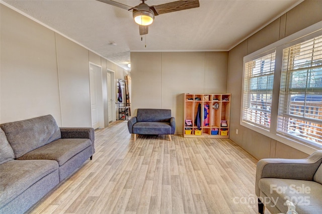 living area with crown molding, ceiling fan, and light wood-type flooring