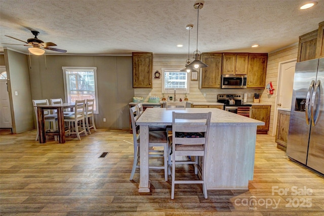 kitchen with a kitchen island, appliances with stainless steel finishes, a breakfast bar, decorative light fixtures, and light wood-type flooring