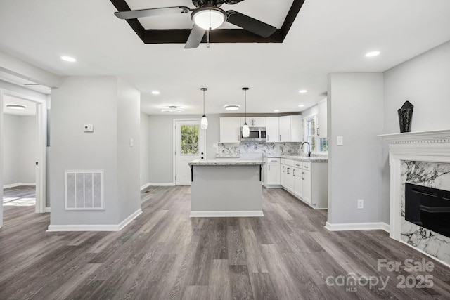 kitchen with light stone counters, hanging light fixtures, white cabinets, a fireplace, and backsplash