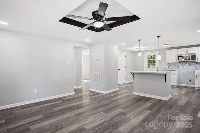 kitchen featuring white cabinetry, dark hardwood / wood-style flooring, hanging light fixtures, a center island, and light stone counters