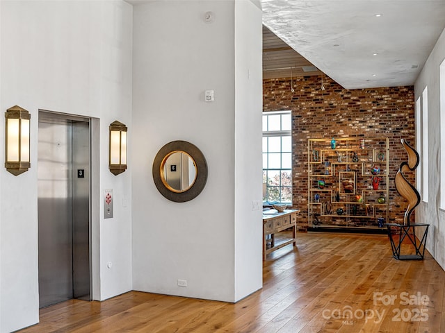 hall with a towering ceiling, wood-type flooring, and elevator
