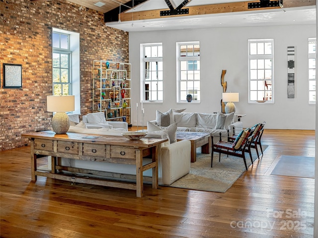 living room featuring lofted ceiling, brick wall, hardwood / wood-style floors, and a wealth of natural light