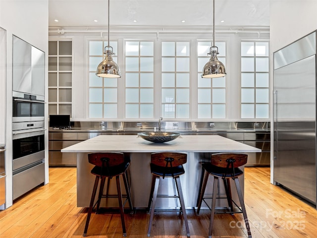 kitchen with hanging light fixtures, appliances with stainless steel finishes, a center island, and light stone counters