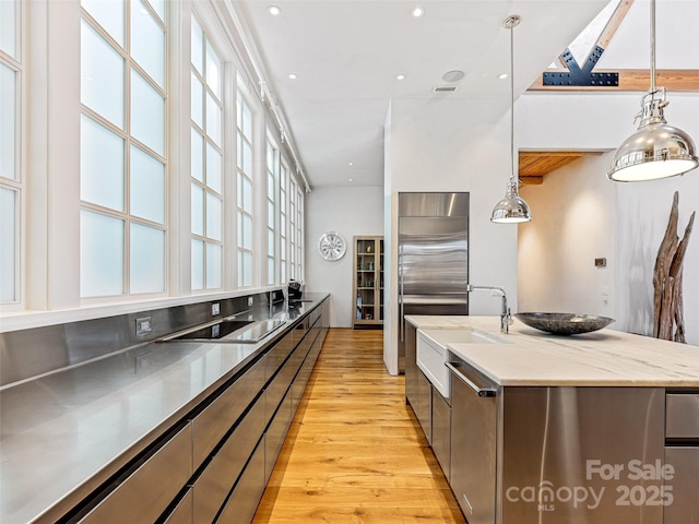 kitchen featuring pendant lighting, stainless steel appliances, light hardwood / wood-style floors, an island with sink, and white cabinets