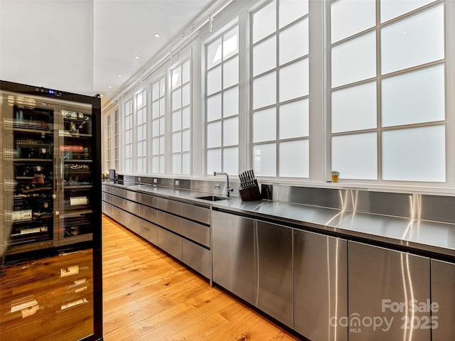 kitchen with sink, stainless steel counters, and light hardwood / wood-style flooring