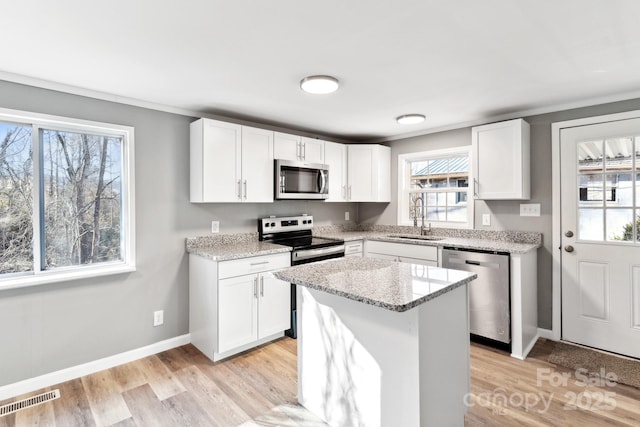 kitchen featuring sink, a center island, appliances with stainless steel finishes, light stone countertops, and white cabinets