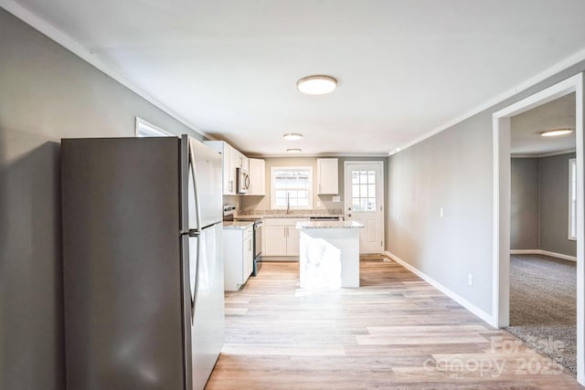 kitchen featuring stainless steel appliances, ornamental molding, white cabinets, and light hardwood / wood-style floors