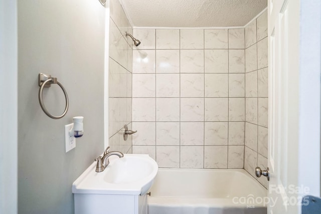 bathroom featuring vanity, a textured ceiling, and tiled shower / bath