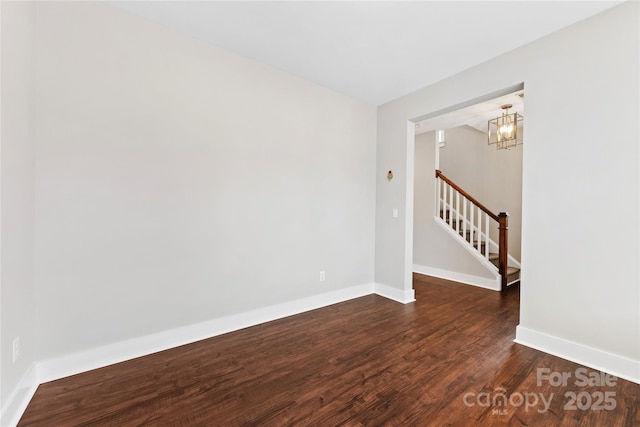 unfurnished room featuring a notable chandelier and dark wood-type flooring