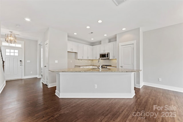 kitchen featuring dark hardwood / wood-style flooring, light stone countertops, an island with sink, and white cabinets