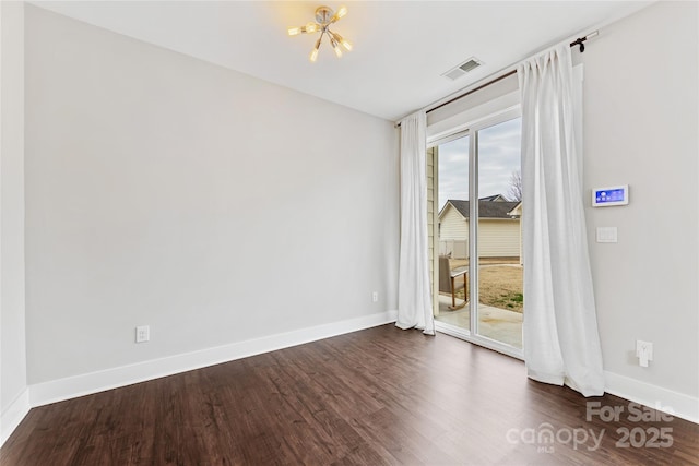 spare room with dark hardwood / wood-style flooring and an inviting chandelier