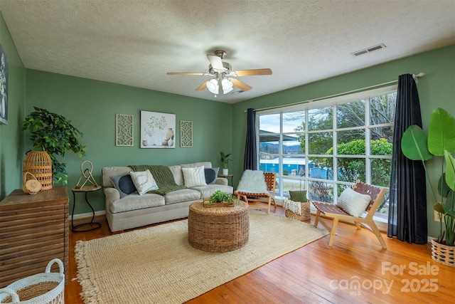 living room featuring visible vents, a ceiling fan, a textured ceiling, wood finished floors, and baseboards