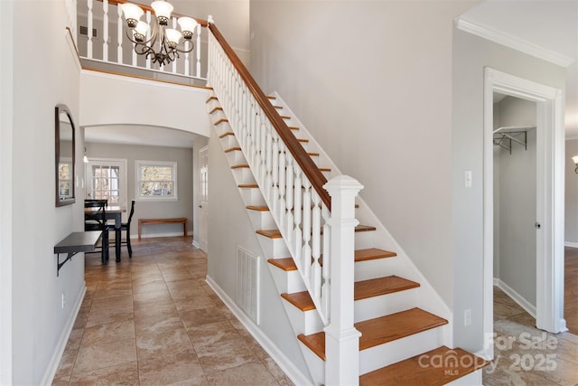 stairway featuring crown molding, a towering ceiling, and a chandelier