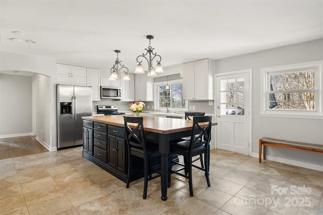 kitchen with appliances with stainless steel finishes, white cabinetry, a center island, wood counters, and decorative light fixtures