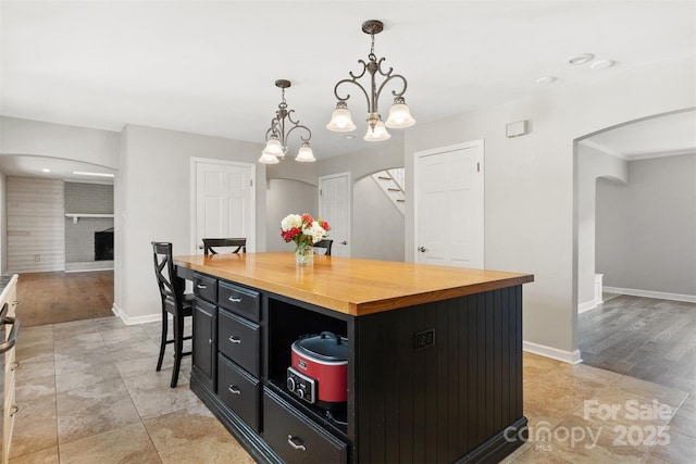 kitchen featuring wooden counters, hanging light fixtures, a kitchen island, a kitchen bar, and a brick fireplace