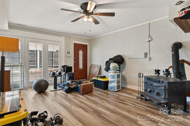 workout area with crown molding, a wood stove, ceiling fan, brick wall, and hardwood / wood-style floors