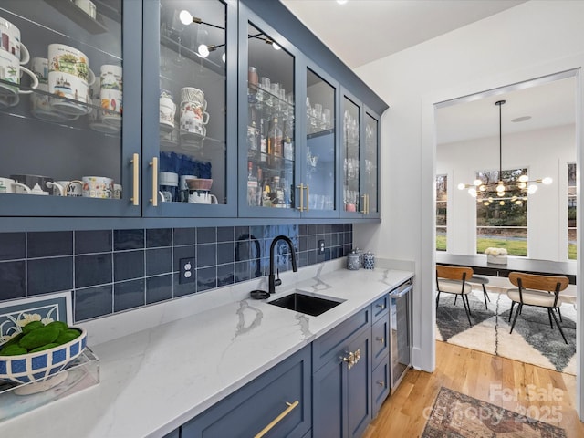 bar with pendant lighting, sink, light stone countertops, blue cabinetry, and light wood-type flooring