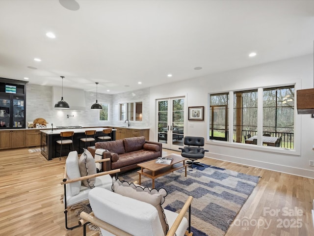 living room with plenty of natural light, sink, light hardwood / wood-style flooring, and french doors