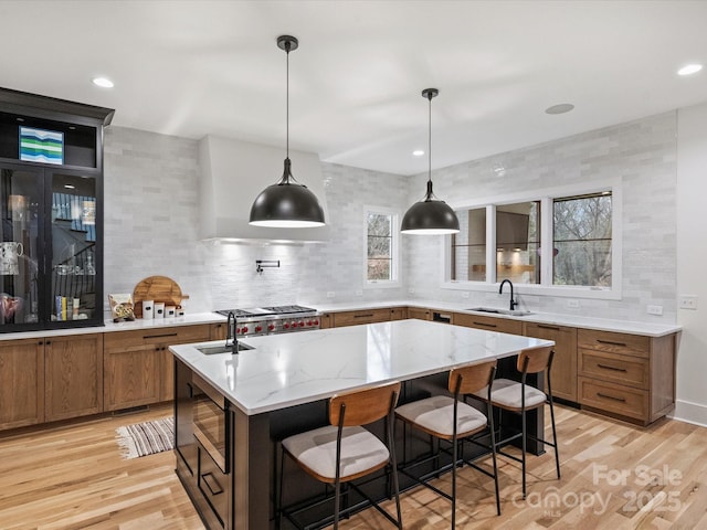 kitchen featuring sink, a breakfast bar, light stone counters, an island with sink, and decorative light fixtures