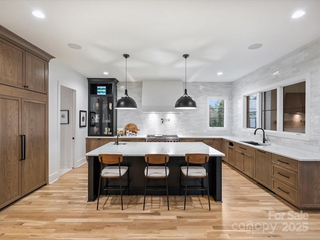 kitchen with a large island, sink, pendant lighting, a kitchen breakfast bar, and wall chimney exhaust hood