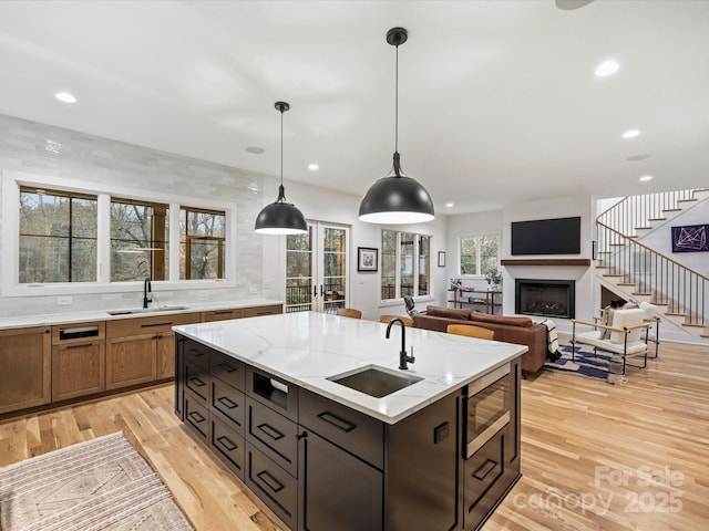 kitchen with built in microwave, sink, a center island with sink, pendant lighting, and light stone countertops