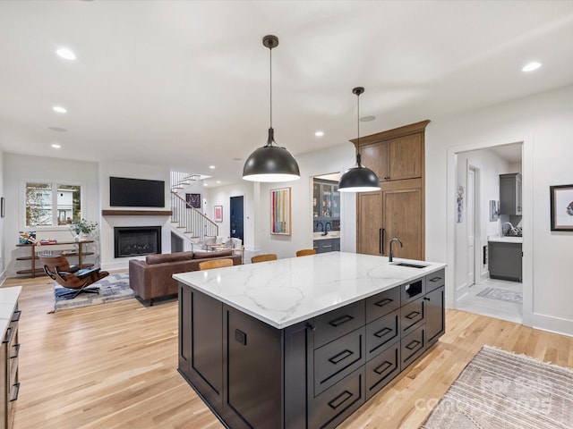 kitchen with hanging light fixtures, an island with sink, light stone countertops, and light hardwood / wood-style floors