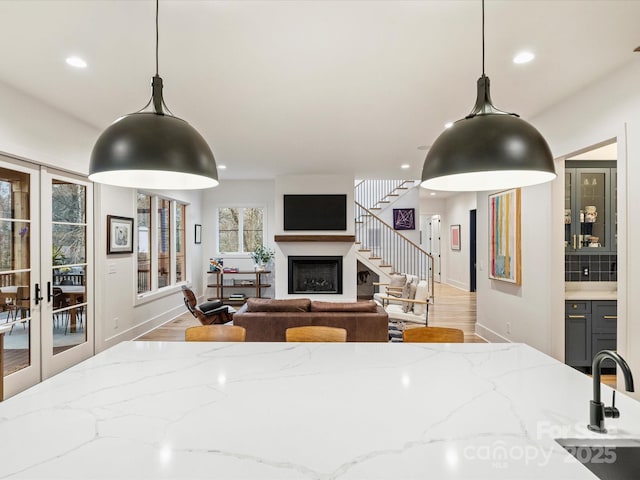 kitchen featuring light stone counters, light hardwood / wood-style floors, french doors, and pendant lighting