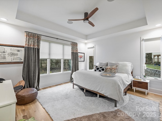 bedroom with a tray ceiling, light hardwood / wood-style flooring, and ceiling fan