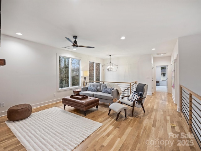 living room featuring ceiling fan with notable chandelier and light hardwood / wood-style flooring