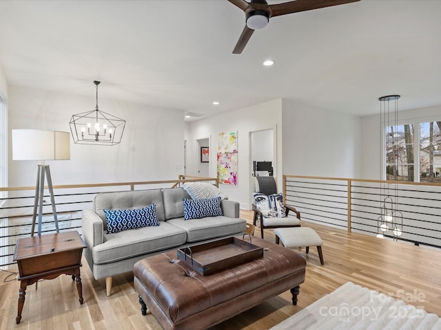 living room featuring ceiling fan with notable chandelier and light wood-type flooring