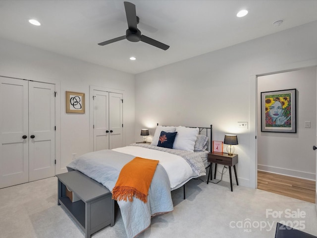 bedroom featuring ceiling fan, light colored carpet, and multiple closets