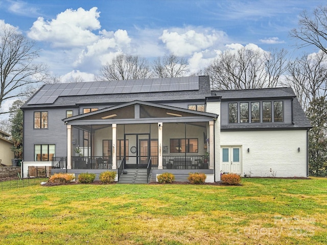 rear view of house with a yard, a sunroom, and solar panels